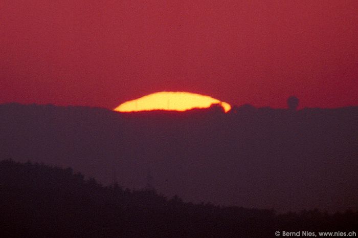 Sonnenuntergang) Noch ein Sonnenuntergang durch ein Refraktor mit f/11 und 1000mm Brennweite aufgenommen. Das runde Dingsbums auf der rechten Seite ist die Radarkuppel vom Flughafen Zürich. — Minolta X-300, Kodak Ektar 100-2, Juli 1992